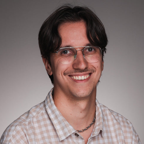 Portraitfoto einer lächelnden Person mit Brille vor neutralem Hintergrund.